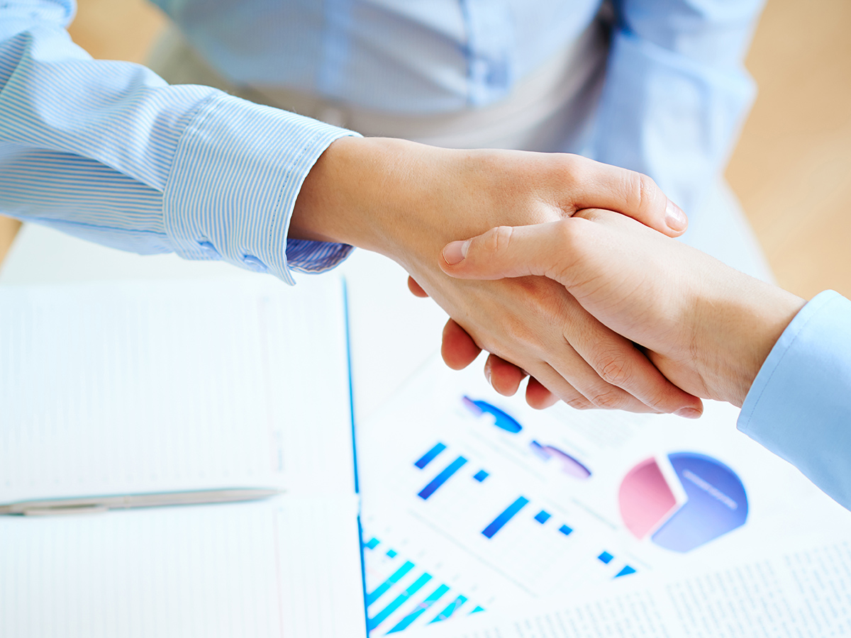 Close-up of female and male handshaking over workplace with business documents